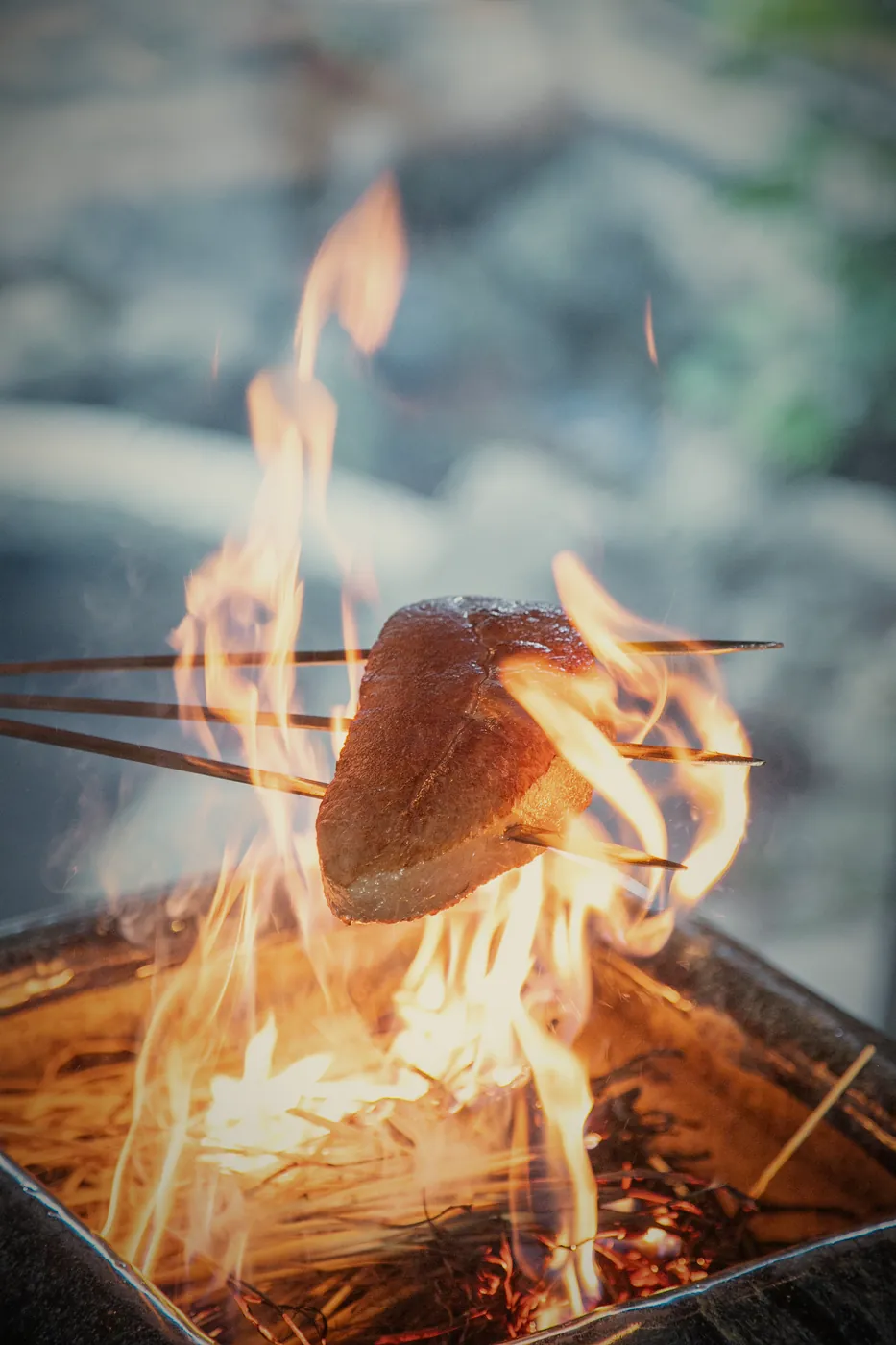 庭を背に、藁の炎で肉を炙る様子